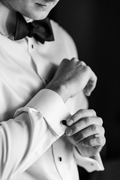 Groom looking down at cufflinks in a black and white photo.