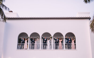bridal party standing on balcony with arms raised above their heads