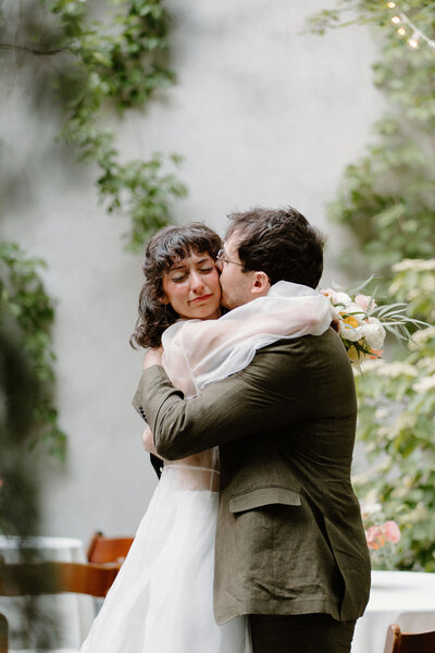 Bride (in whimsical white wedding dress) and Groom (in green suit) embracing after their wedding ceremony