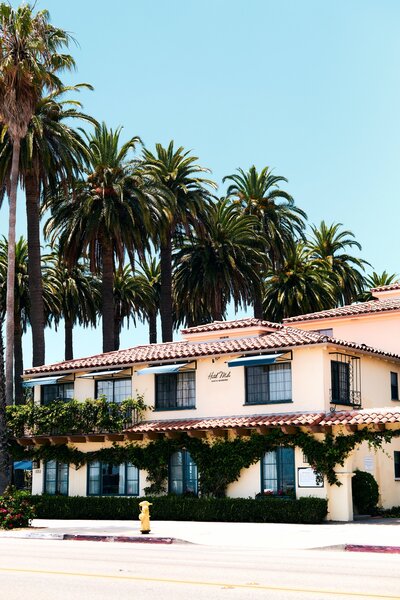 A two story Santa Barbara style hispanic building on a sunny day. Palm trees behind.