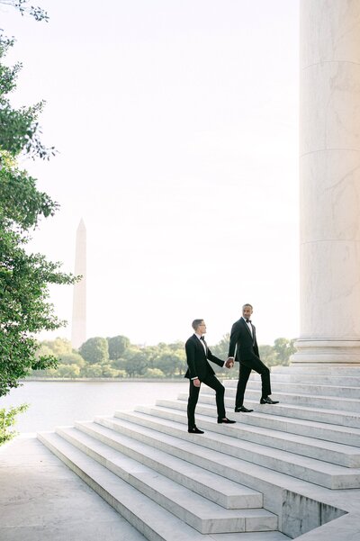 Same sex couple walking up the step of the Jefferson Memorial with the Washington Monument in the background