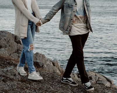 Storytelling photographer captures engaged couple walking along the rocks holding hands during their engagement session at Castle Rock Marblehead, MA