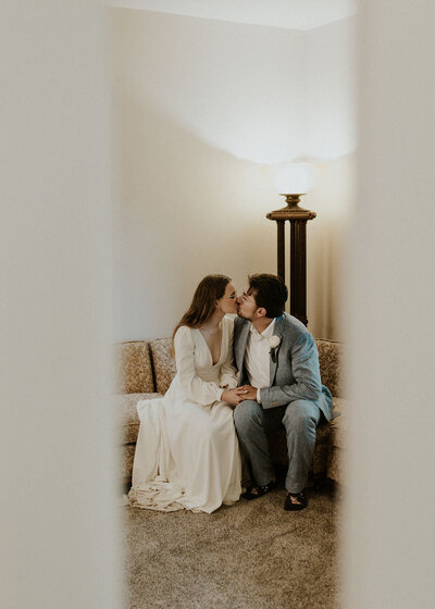 Bride and groom sitting on a couch in a corner kissing