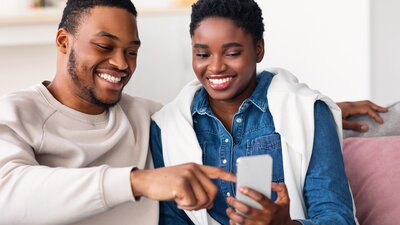 Black couple on couch looking at phone together and smiling.