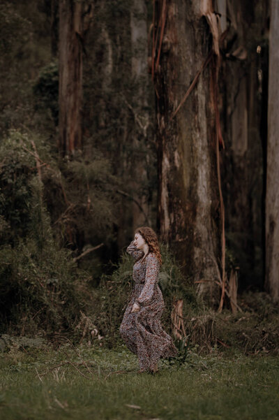 Girl in long floral dress walking from right to left in front of australian forest
