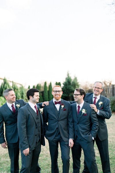 Groom and Groomsmen in dark grey suites with burgundy and cream details on lawn at the Cordelle