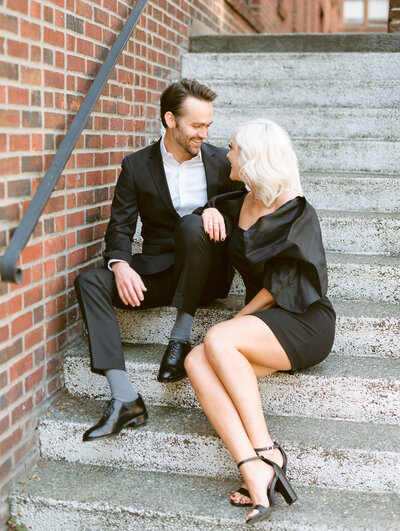 City Engagement Photograph on steps while wearing black tuxedo and black cocktail dress