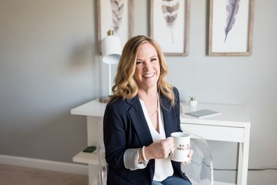 Nashville business coach wearing a navy blazer sitting at a white desk with a white coffee mug that says Goal Digger