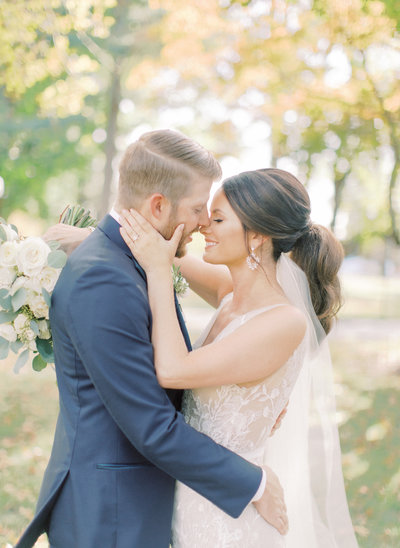 bride embraces grooms face as they smile at each other forehead to forehead