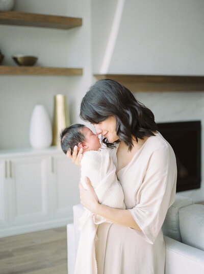 A mother in neutral clothes holds up her newborn baby during her Edmonton newborn photography session