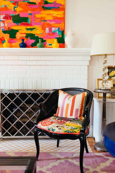 A white brick fireplace with colorful artwork and black chair.