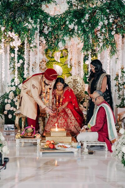 A bride and groom performing a ritual during a traditional indian wedding ceremony, with a priest overseeing the process.