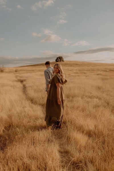 A couple walking through a field of tall grass.