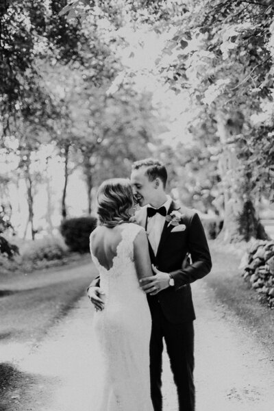 The groom embraces his bride on a tree-lined path.
