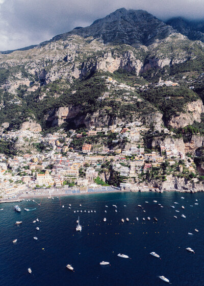 Aerial view of Positano along the Amalfi Coast, with boats scattered across the deep blue water.
