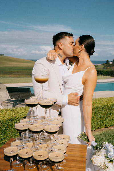 Georgia and Joe kissing behind their espresso martini tower, wedding at Seacliff House, Gerringong