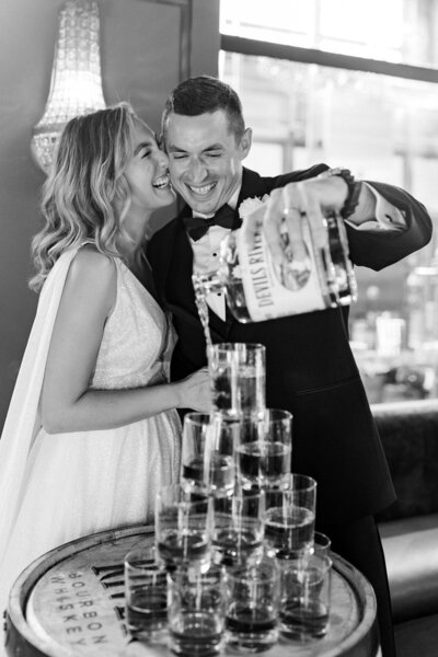 bride and groom giggle pouring whisky