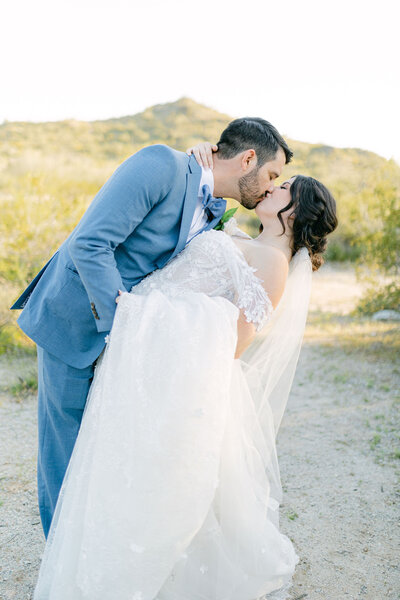 Romantic desert wedding: Groom tenderly dips bride, sealing the moment with a kiss against a stunning mountainous backdrop