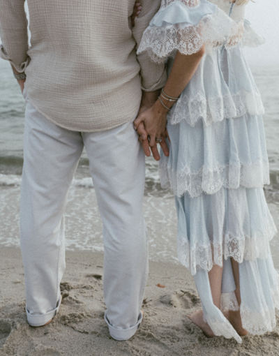 A woman in a blue and white lace dress wrapping arms around man at the beach