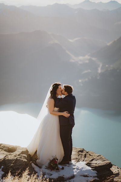 bride and groom kissing on a mountains edge overlooking a lake