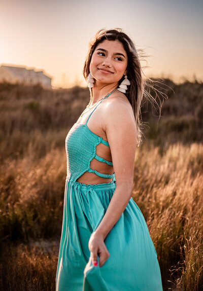 A Santa Fe senior poses for portraits at a Galveston beach while wearing a turquoise dress.