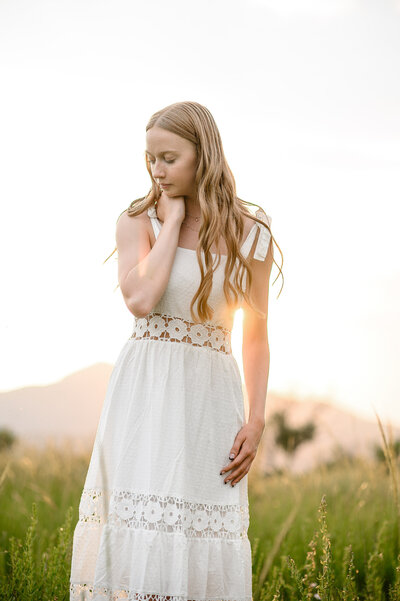 Senior outfit ideas with a young girl with red hair standing in the setting sun with a white dress with crochet details