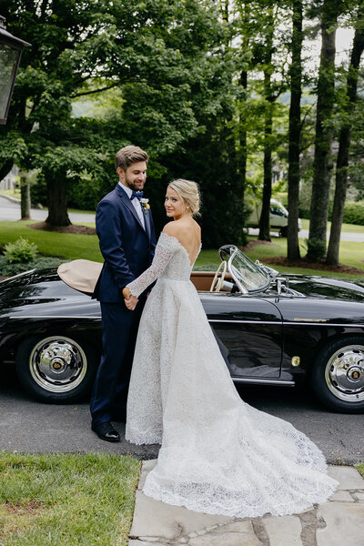Sophisticated bride and groom pose for portrait in front of vintage coupe