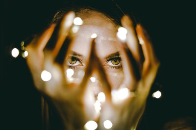A mysterious woman with amber eyes gazes through a string of lights around her fingers.