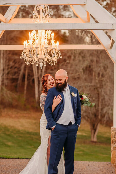photo of bride and groom cuddling under a chandelier