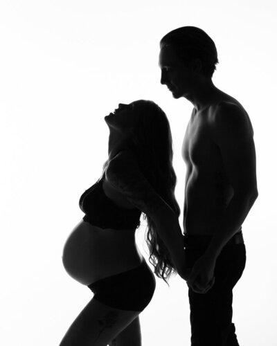 Fort Mill, SC husband and wife silhouette  maternity portrait in black and white mom to be is leaning back holding dad to be's hands and the enphasis is on her shape and the connection between the expecting parents.