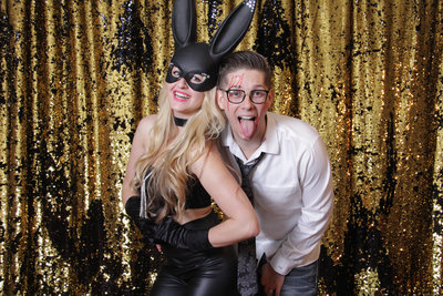 couple posing front of a gold and black backdrop having bunny ears
