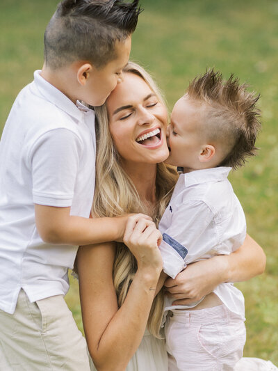 A mom laughing in the middle of her two boys giving her a kiss on the cheek