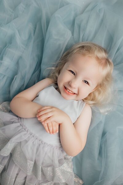 Little girl smiling and laying on blue tulle by baby photographer nj