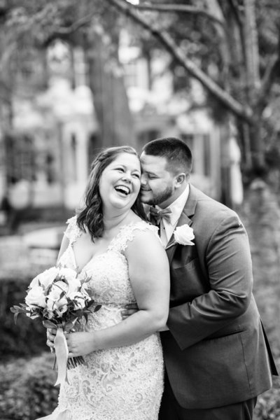 black and white photo of bride laughing and groom  behind her with his nose at her temple