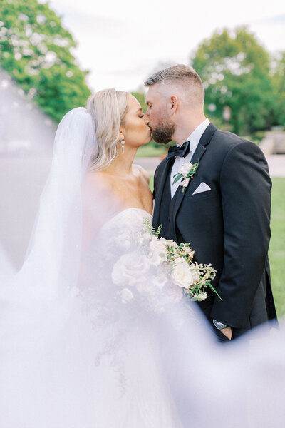 A bride and groom kissing with veil blowing in the wind