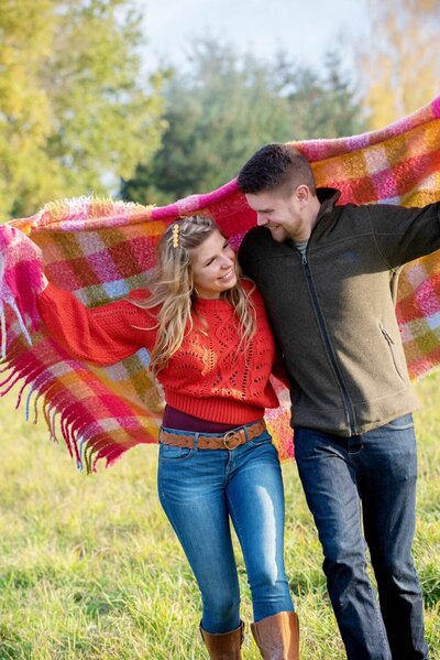 a couple in bright colors run holding a vibrant blanket over their heads