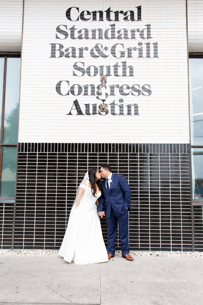 An Austin-based wedding photographer captures a couple's romantic kiss in front of a building adorned with a central standard sign.