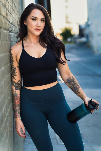 brand photo of a fitness coach posing leaning on the wall, water bottle in her hands