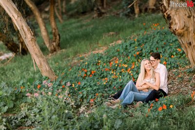 Engaged couple cozy up as they sit amongst the flowers at the Gum Grove Park in Seal Beach