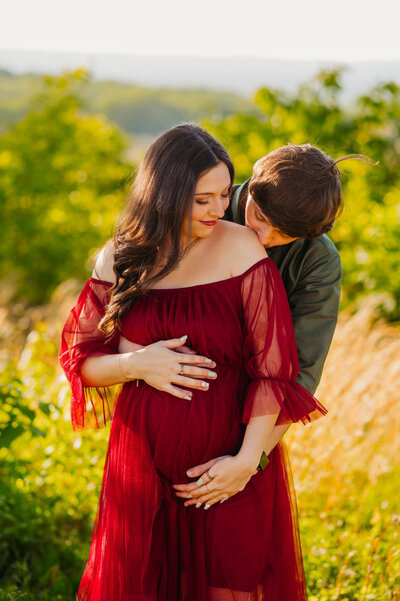 photo of pregnant woman holding her belly as husband kisses her shoulder