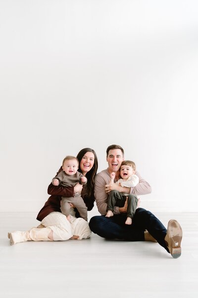 Family photo of mother, father, and two sons, laughing in the floor of studio