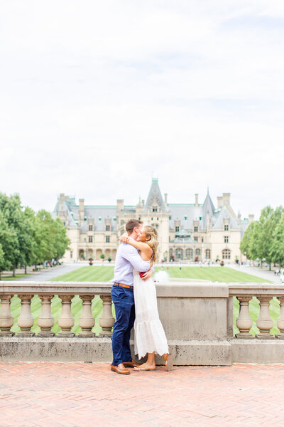 girl in white dress and guy in dress clothes hugging with biltmore estate in background
