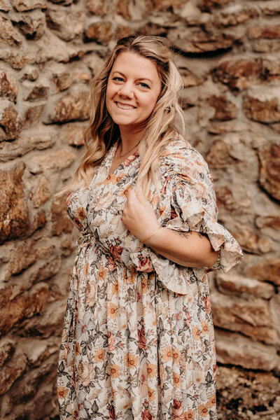 Kate McCord owner of the business smiling in a floral dress in front of a stone wall during family photos in Harrisburg. PA