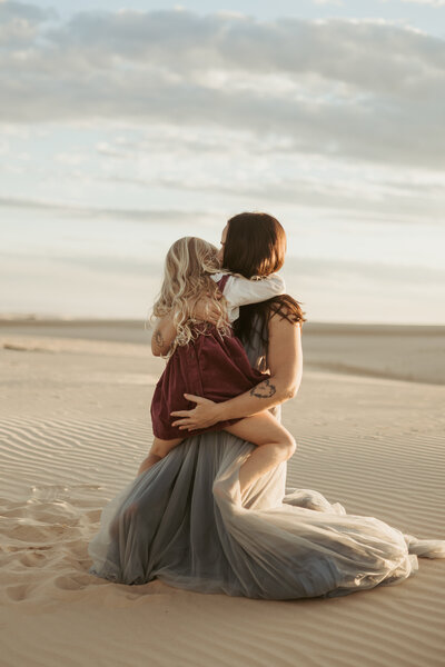 Mum in a beautiful tulle dress cuddling her daughter and giving her a kiss.