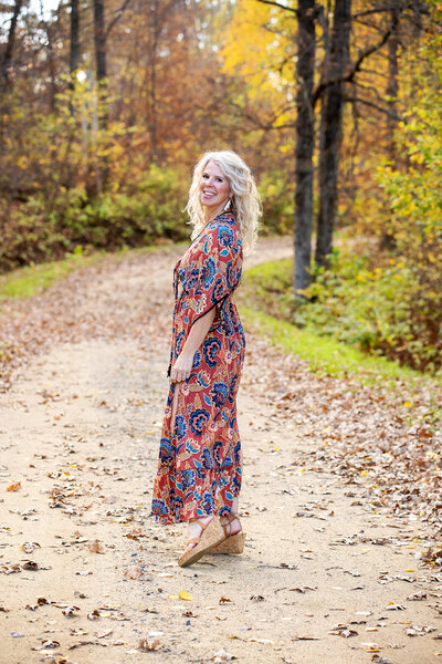 The owner of Studio 64 Photography in Akeley, Minnesota walking down her driveway during the fall looking back smiling.