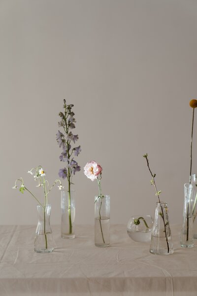 Flowers in glass vased ontop of a table with a linen table cloth.