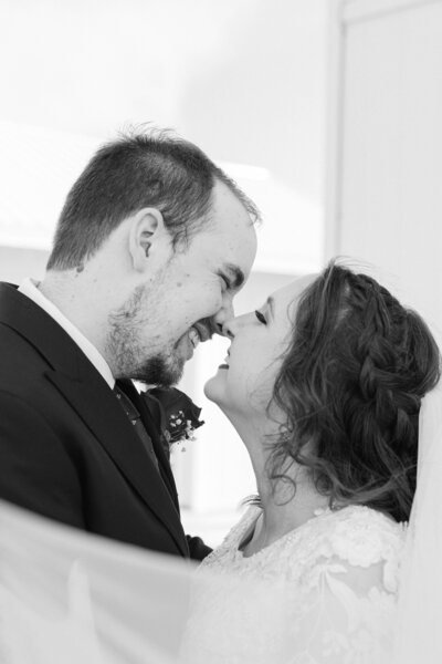 A portrait of the bride and groom, leaning towards each other, sharing sincere smiles as they gaze into each other's eyes, capturing a moment of genuine joy