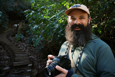 Jake Ford wearing a Patagonia hat and holding a film camera, capturing weddings with a documentary eye.