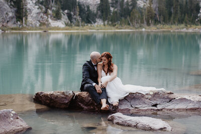grand Teton wedding with bride and groom sitting on the rocks in a lake of the mountains kissing photographed by jackson hole photographers