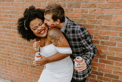 Man kisses his wife while they share beers together.